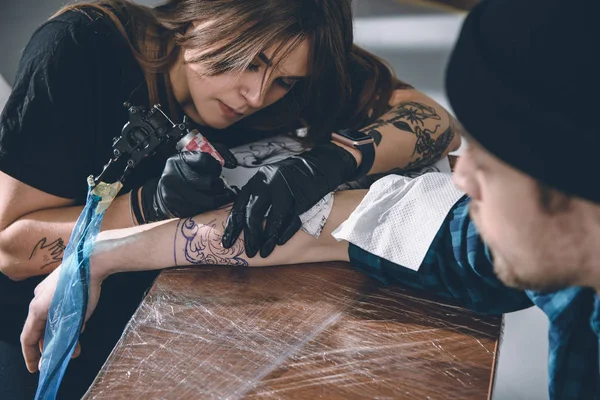 Mestre de tatuagem feminina em luvas trabalhando em peça de braço em estúdio — Fotografia de Stock