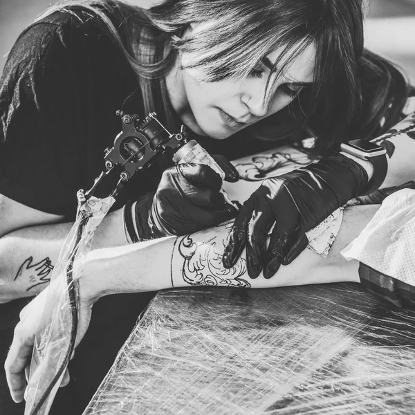 Черно-белое фото сконцентрированной художницы в перчатках, работающей над татуировкой в студии — стоковое фото