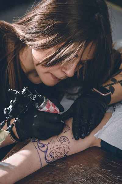 Artista femenina concentrada en guantes trabajando en el tatuaje de la pieza del brazo en el estudio - foto de stock