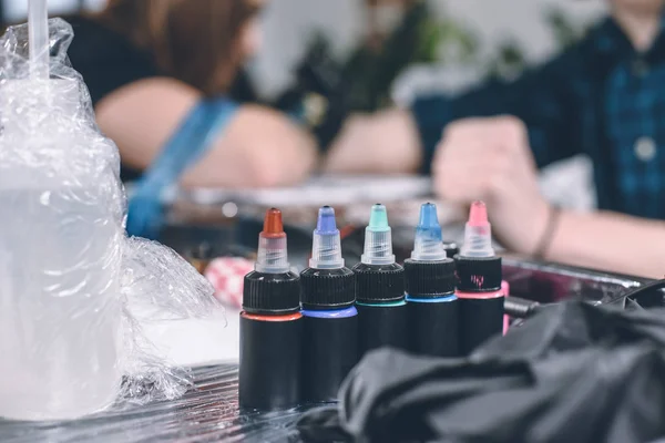 Botellas de tinta en la mesa delante del artista del tatuaje de trabajo - foto de stock