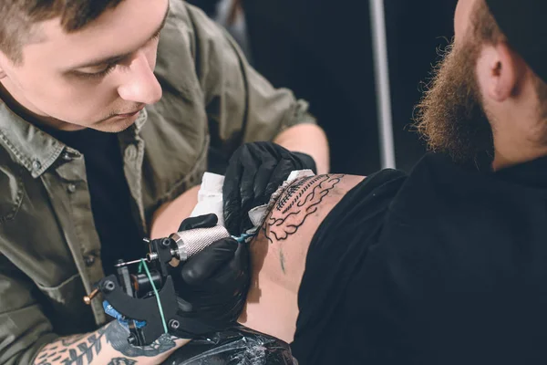 Artista del tatuaje y hombre barbudo durante el proceso de tatuaje en el estudio - foto de stock