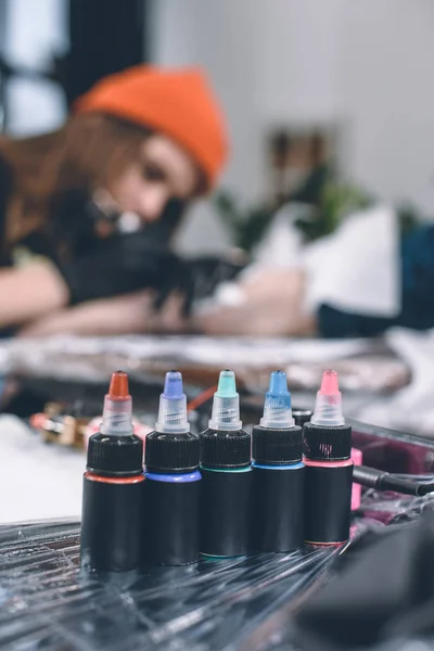Bottles of ink in front of working tattoo master — Stock Photo