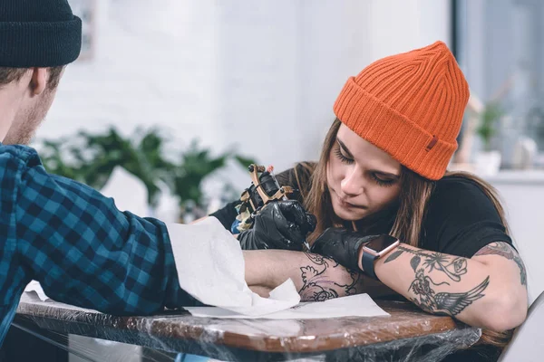 Jeune homme et maître de tatouage féminin pendant le processus de tatouage en studio — Photo de stock