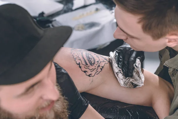 Maestro en guantes trabajando en tatuaje de hombro en estudio - foto de stock