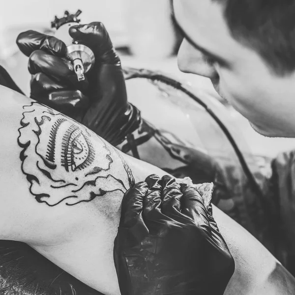 Foto en blanco y negro del artista del tatuaje en guantes trabajando en pieza de hombro en el estudio - foto de stock