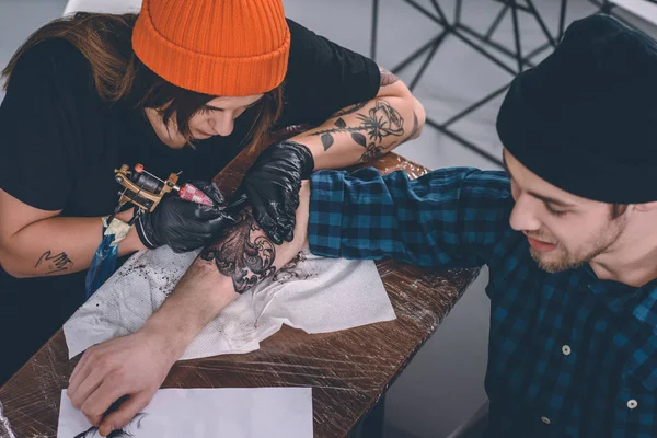 Молодой человек и женщина-татуировщик во время процесса татуировки в студии — стоковое фото