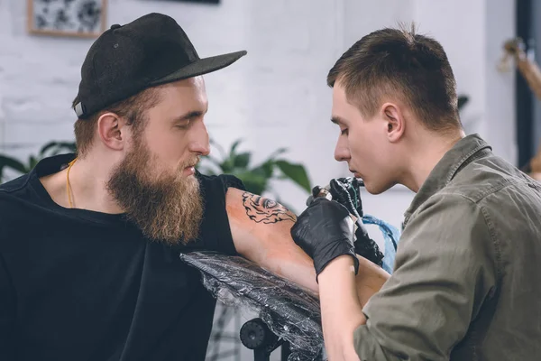 Tattoo artist and bearded man during tattooing process in studio — Stock Photo