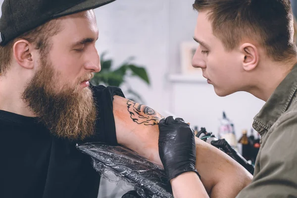 Uomo barbuto e maestro del tatuaggio durante il processo di tatuaggio in studio — Foto stock