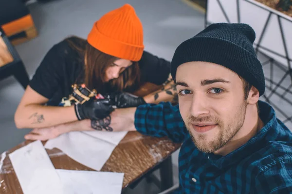 Uomo sorridente e maestro del tatuaggio durante il processo di tatuaggio in studio — Foto stock