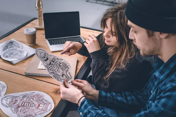 Pareja joven eligiendo diseño de tatuaje en estudio - foto de stock