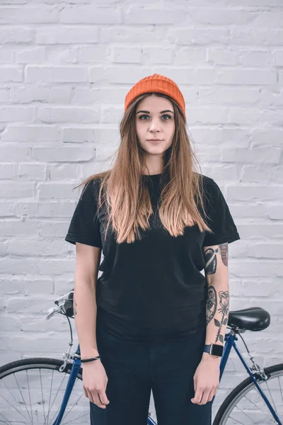 Young girl with tattooed arm standing next to bicycle by the wall — Stock Photo