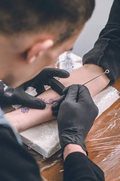 Artista del tatuaje en guantes trabajando en pieza de brazo femenino en estudio - foto de stock