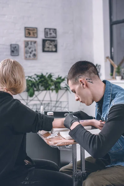 Girl in tattoo studio with artist working — Stock Photo