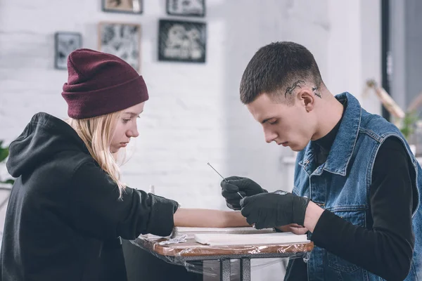 Tätowiermeister in Handschuhen arbeitet an Armstück im Studio — Stockfoto