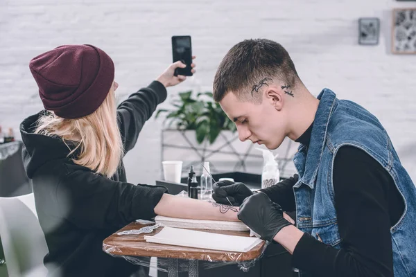 Mädchen macht Selfie von Tätowierungsprozess im Studio — Stockfoto