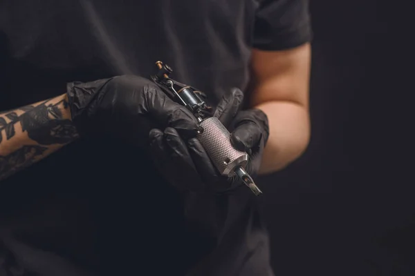 Maestro del tatuaje en guantes que sostienen la máquina de tinta aislada en negro - foto de stock