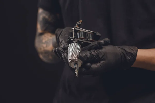 Manos masculinas en guantes que sostienen la máquina del tatuaje aislada en negro - foto de stock
