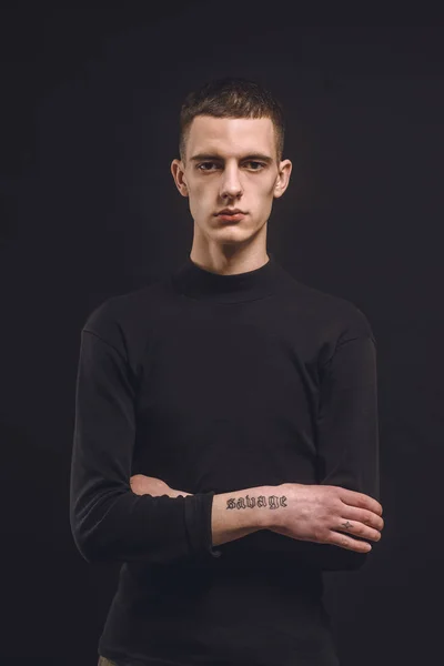 Hombre seguro con los brazos tatuados aislados en negro - foto de stock