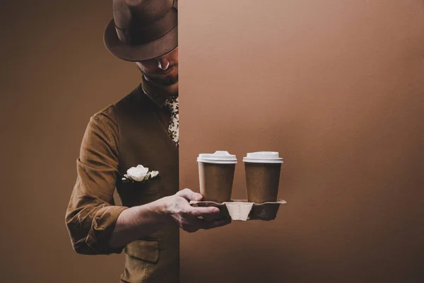 Uomo elegante in abiti casual che tengono il caffè in tazze di carta isolate su marrone — Foto stock