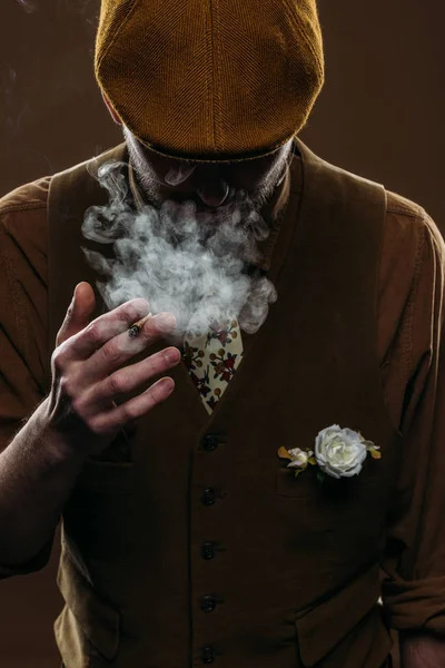 Man wearing corduroy vest and flat cap smoking isolated on brown — Stock Photo