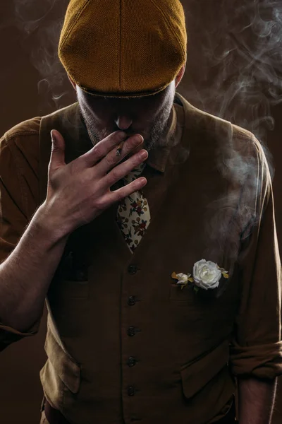 Stylish man in flat cap smoking cigarette isolated on brown — Stock Photo