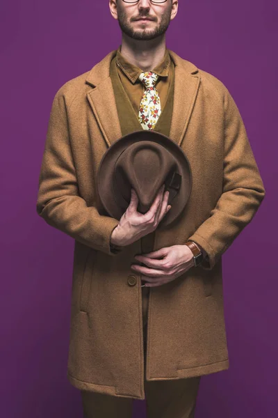Стильный мужчина в пальто со шляпой в руках изолированы на фиолетовый — стоковое фото