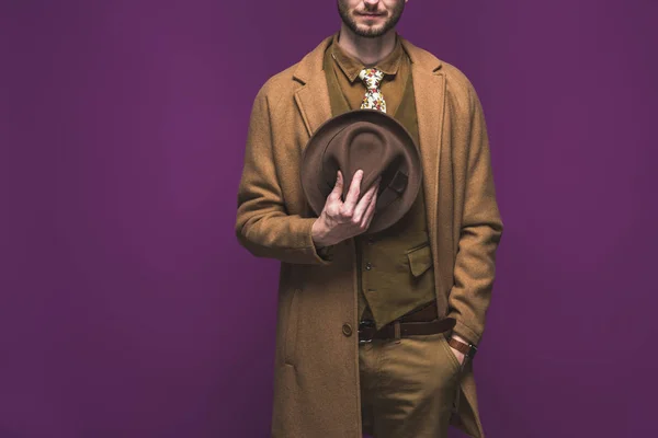 Uomo elegante che indossa cappotto e tenendo il cappello isolato su viola — Foto stock