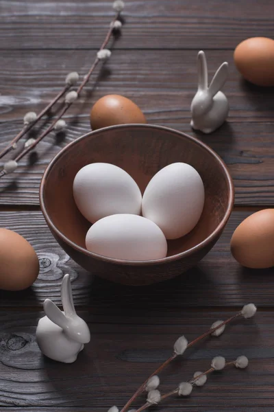 Uova di pollo in ciotola e conigli pasquali sul tavolo di legno — Foto stock