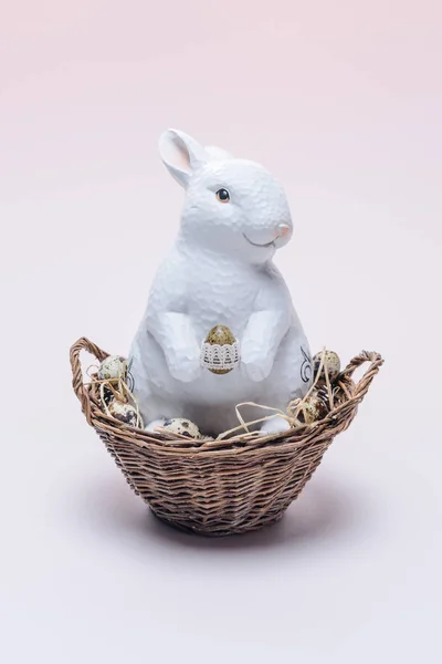 Ester rabbit with quail eggs and straw in basket on beige — Stock Photo