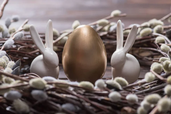 Huevos de pascua dorados y conejos en amentos anidan en la mesa - foto de stock