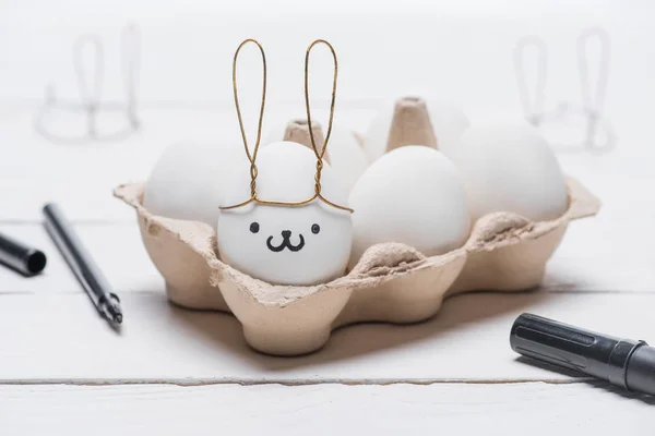 Oeuf de poulet de Pâques avec des oreilles souriantes et lapin dans le bac à œufs sur la table — Photo de stock