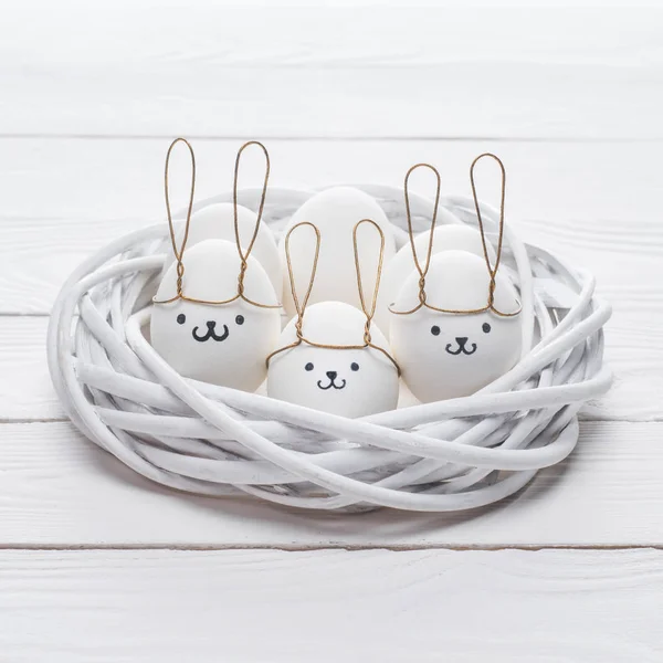 Oeufs de poulet de Pâques avec des sourires et des oreilles de lapin dans le nid sur la table — Photo de stock