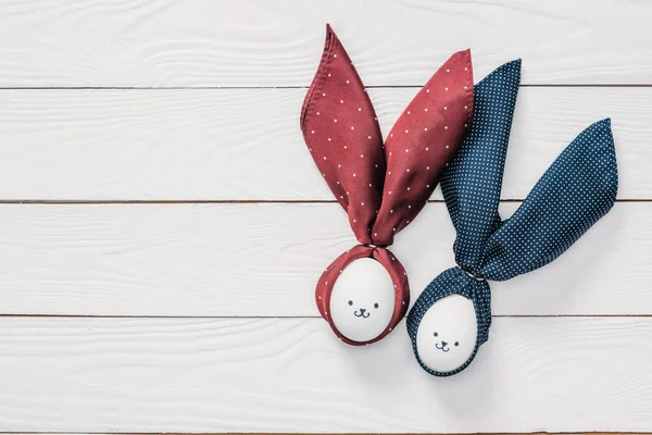 Vista superior de huevos de pollo de Pascua con emoticonos y orejas de conejo en mesa de madera - foto de stock