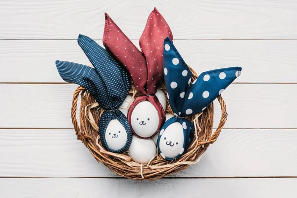 Vista superior de huevos de pollo de Pascua con emoticonos y orejas de conejo en cesta - foto de stock