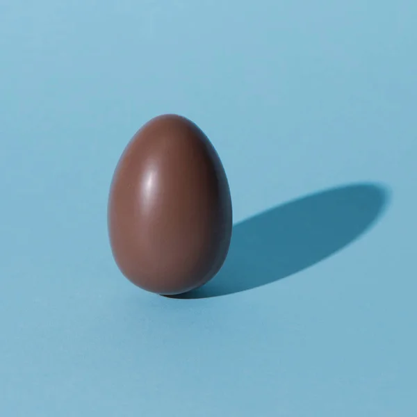 Одно шоколадное пасхальное яйцо на голубой поверхности — стоковое фото