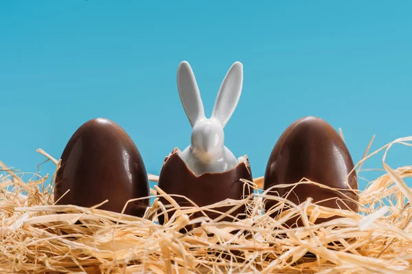 Easter bunny in chocolate eggs on straw isolated on blue — Stock Photo