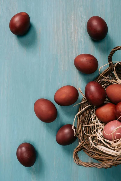 Vista superior de la cesta de Pascua con huevos pintados y paja en la mesa - foto de stock