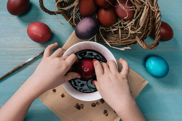 Cropped image of kid painting easter eggs in cup with paint at home — Stock Photo