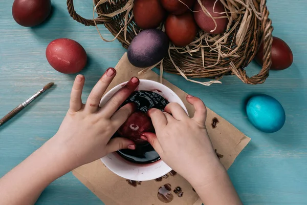 Imagen recortada de niño pintando huevos de Pascua en taza con pintura - foto de stock