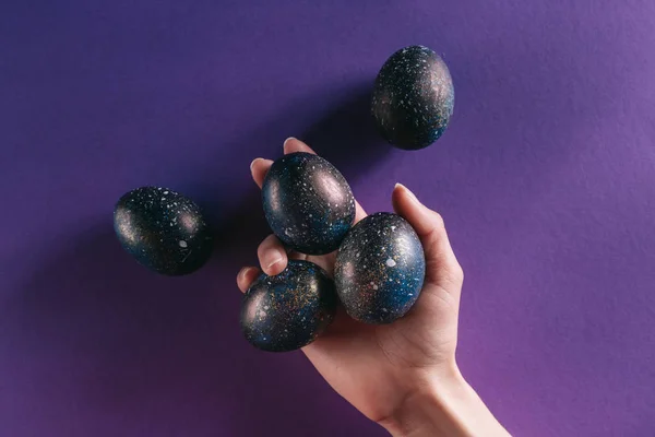 Imagen recortada de la mujer sosteniendo huevos de Pascua pintados por encima de la superficie violeta - foto de stock