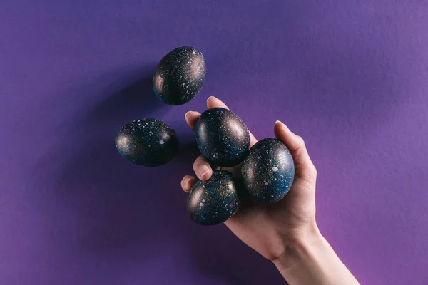 Cropped image of woman holding painted easter eggs above violet surface — Stock Photo