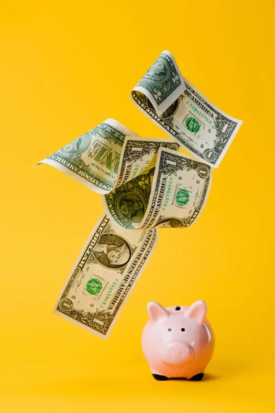 Close up view of pink piggy bank and falling dollar banknotes isolated on yellow — Stock Photo