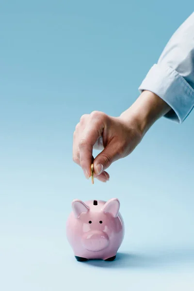 Vista parcial del hombre poniendo moneda en la alcancía rosa aislado en azul - foto de stock