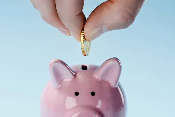 Partial view of man putting coin into pink piggy bank isolated on blue — Stock Photo