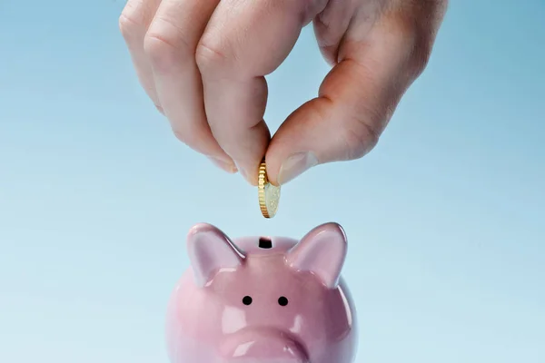 Vista parcial del hombre poniendo moneda en la alcancía rosa aislado en azul - foto de stock