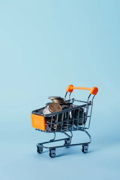 Close up view of little shopping trolley full of coins isolated on blue — Stock Photo