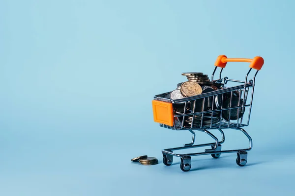 Vista de perto de pouco carrinho de compras cheio de moedas isoladas em azul — Fotografia de Stock