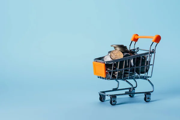 Vista de perto de pouco carrinho de compras cheio de moedas isoladas em azul — Fotografia de Stock