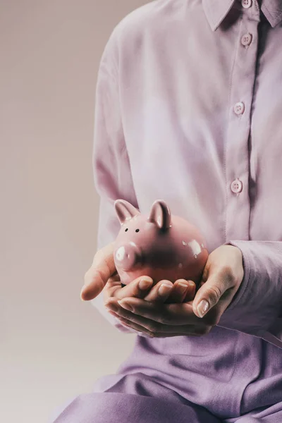 Partial view of woman holding pink piggy bank in hands isolated on lilac — Stock Photo