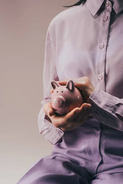 Partial view of woman holding pink piggy bank in hands isolated on lilac — Stock Photo